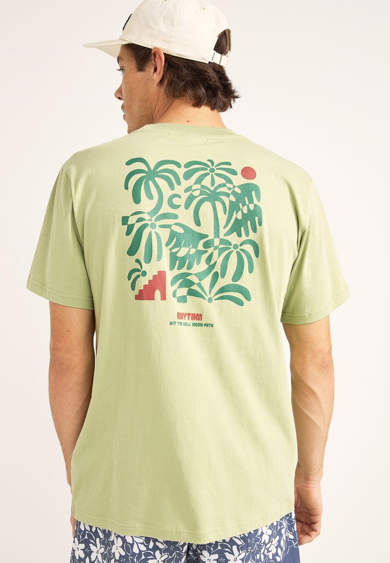 Camiseta ligera verde con un gran gráfico de palmeras, un sol y escaleras en verde oscuro y rojo. Material de algodón suave con mangas cortas.