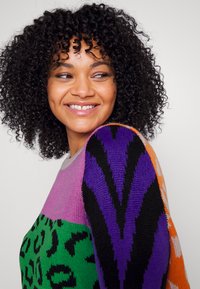 Knit sweater featuring a color-block design with light pink, green, purple, and orange sections. Patterns include leopard spots and zigzags.