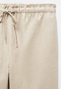 Pantalons beiges avec une texture brillante, dotés d'une taille élastique et d'un cordon de serrage. Tissu lisse et léger avec un design à jambes droites.
