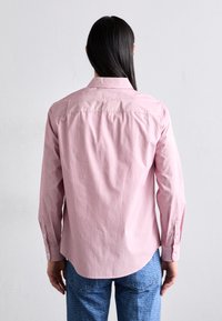 Lyserosa langermet skjorte med krage med knapper, rett snitt og synlige sømdetaljer. Båret med blå mønstret denim.
