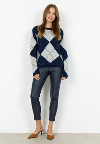 Marineblau und hellgrau gestreifter Pullover mit lockeren Ärmeln, kombiniert mit schwarzen, eng anliegenden Leggings in Lederoptik und beigefarbenen, spitzen Absätzen.