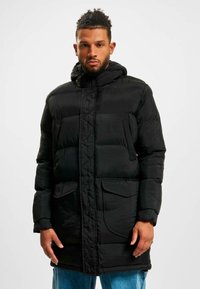 Geacă puffer neagră cu glugă, cu un design matlasat, fermoar frontal și două buzunare laterale. Fabricată dintr-un material neted, rezistent la apă.