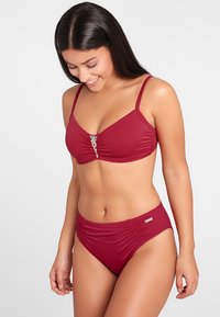 Set bikini rosso con un design texturizzato e arricciato. Il top presenta un accento decorativo al centro, mentre i pantaloni hanno un taglio a vita alta.