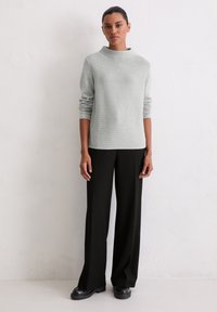 Jasnoszary sweter z prążkowanego dzianiny z wysokim kołnierzem i długimi rękawami, w połączeniu z czarnymi, szerokimi spodniami i czarnymi butami na platformie.