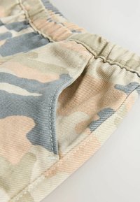 Shorts de camouflage dans des teintes beige, gris et pêche clair ; dotés d'une taille élastique et d'une poche latérale avec une finition en tissu texturé.