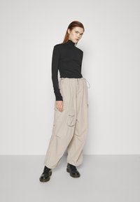 Svart langermet turtleneck topp parret med beige cargo-bukser som har store sidelommer, innsnevret midje og svarte snørebåndsstøvler.