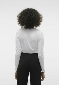 Maglietta bianca a maniche lunghe con una texture liscia, abbinata a pantaloni neri su misura, vista da dietro. Design semplice senza motivi visibili.