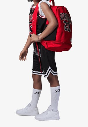 Dziecko ubrane w czarno-biały strój koszykarski Michaela Jordana, z białymi skarpetkami i butami, niosące czerwony plecak Jordan 23.