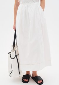 Gonna bianca alla caviglia con vita arricciata, abbinata a una borsa a tracolla bianca e nera e sandali neri con zeppa. Materiali morbidi e lisci.