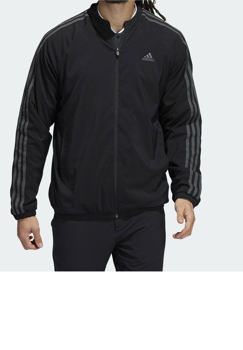 Veste de sport noire avec fermeture zippée à l'avant, col montant et poignets élastiques, ornée de trois bandes grises sur chaque manche. Texture lisse.