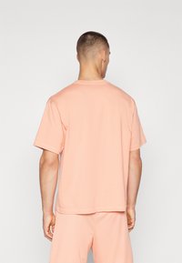 Tricou cu mânecă scurtă din bumbac moale piersică, cu o croială lejeră, guler rotund și detalii de cusătură minime la margine și la mâneci.