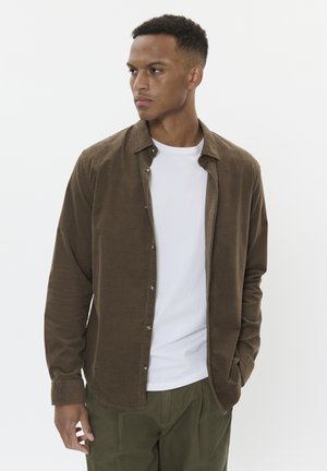 Braune Button-Up-Hemd aus weichem Material, mit klassischem Kragen, langen Ärmeln und kontrastierenden Knöpfen, über einem weißen T-Shirt getragen.