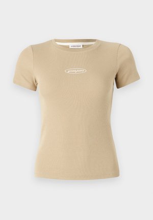 T-shirt beige à manches courtes avec un col rond et un logo "guess jeans" blanc sur le devant. Texture de tissu douce.