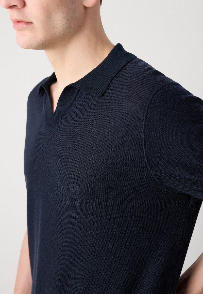 Polo bleu marine avec une finition texturée, manches courtes et col traditionnel, doté d'un design en V pour un ajustement moderne.