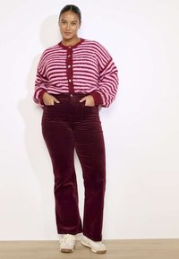 Cárdigan de punto a rayas en tonos rosa y burdeos con botones, combinado con pantalones de pana burdeos acampanados y zapatillas color crema.