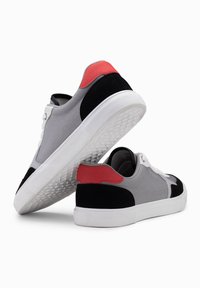 Šedé a černé tenisky s červenými akcenty, s textilním svrškem, gumovou podrážkou a texturovaným patním dílem. Šněrovací design s kontrastními barvami paty.