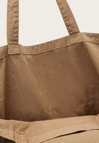 Beige színű pamut táska széles varrott fülekkel és látható varrásokkal, amely bemutatja a belső és a felső szélek részleteit.