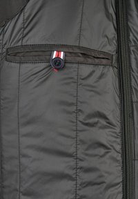 Donkergrijze gewatteerde jas met een ritssluiting, voorzien van een knoopzak met een rood, wit en blauw gestreepte accent. Gestructureerde stof.