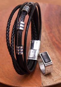 Zwarte leren armband met geweven textuur en zilveren accenten, samen met een metalen ring met een zwarte horizontale streep.