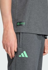 Ropa deportiva gris con una textura suave. Los detalles notables incluyen una etiqueta negra con texto verde y un logo de Adidas en verde menta.