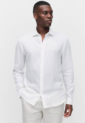 Chemise blanche en lin à manches longues avec un col boutonné, offrant une texture légère et une coupe droite. Sans motifs ni embellissements.