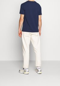 Granatowa koszulka z okrągłym dekoltem, białe luźne spodnie i wielokolorowe trampki. Prosty wzór, materiał bawełniany i podwinięte mankiety spodni.