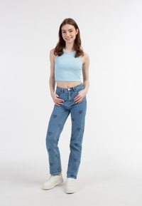 Top corto a coste blu chiaro, jeans a vita alta blu con motivi a cuore e sneakers bianche. Tessuto morbido, vestibilità casual e design vivace.