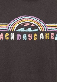 Grå bomullströja med en färgglad retrodesign som har en regnbågsbåge ovanför blå vågor och texten "BEACH DAYS AHEAD" i livliga bokstäver.