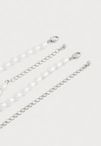 Duplex colares de corrente prateada com pérolas ovais brancas e fechos de lagosta sobre um fundo branco.