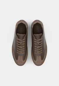 Brown sneakers featuring a mix of smooth and suede textures, rounded toe, and flat laces. Accents in darker shades and minimal branding.