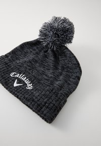 Melnā adīta cepure ar teksturētu rakstu, ar lielu pelēku pom-pomu un baltu "Callaway" izšūtu uzmalu.