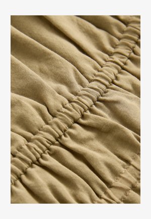 Tejido de color arena con textura gathered, mostrando costuras elásticas horizontales y una superficie suave, enfatizando la flexibilidad y suavidad.