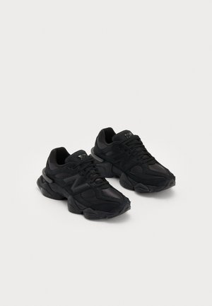 Baskets de sport noires avec une tige texturée, arborant un logo "N" en relief, une semelle rembourrée et une silhouette moderne et épurée.