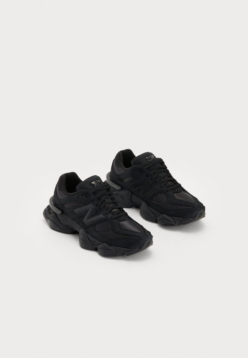 Baskets de sport noires avec une tige texturée, arborant un logo "N" en relief, une semelle rembourrée et une silhouette moderne et épurée.