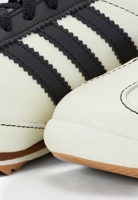 Witte leren schoenen met zwarte zigzagstrepen, textuurelementen en rubberen zolen. Close-up benadrukt het unieke ontwerp en het kleurcontrast.