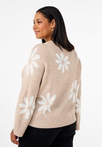 Beiger Pullover mit weißen Gänseblümchenmustern. Weiche Textur, lange Ärmel und gerippten Saum. Entworfen für eine lockere Passform.