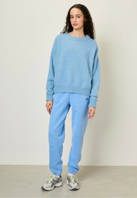 Ljusblå stickad tröja med avslappnad passform och ribbade muddar, i kombination med matchande lössittande blå sweatpants. Skor: grå sneakers.