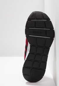 Svart gummisul med strukturerad mönstring, med röda mesh-accenter och tre svarta ränder. "adidas"-logotypen är synlig på hälen.