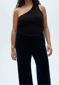 Musta ribattu yhdelle olkapäälle tarkoitettu toppi yhdistettynä tummansinisistä leveälahkeisiin samettihousuihin. Kangas on sileäpintaista ja siluetti myötäilee vartalon muotoa.