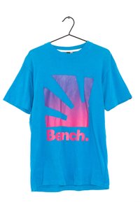 Sininen puuvillapaita lyhyillä hihoilla, jossa on liukuvärjätty auringonsäteet tulostus purppurasta vaaleanpunaiseen ja sana "Bench." rohkealla vaaleanpunaisella fontilla.