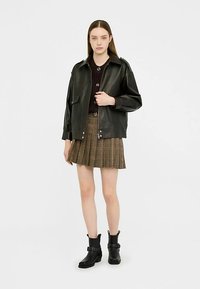 Veste en cuir noir à coupe décontractée, deux poches avant, associée à une jupe écossaise marron et des bottines noires.