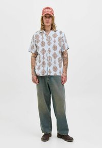 Chemise légère à manches courtes de couleur bleu clair avec un motif géométrique marron, associée à un jean en denim délavé à coupe ample et des chaussures marron foncé.