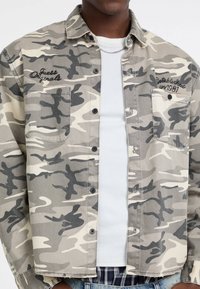 Camouflage overhemd in beige en grijs katoen, met twee borstzakken, geborduurde branding en een relaxte pasvorm.