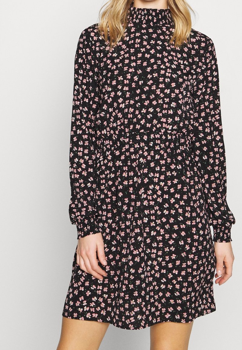 Robe noire à fleurs avec manches longues, dotée d'un col montant, d'une taille cintrée et de petits motifs de fleurs roses et blanches tout au long.