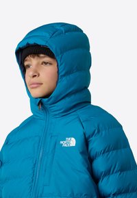 Kék pufi dzseki kapucnival, cipzáras elülső résszel, steppelt mintázattal és jól látható logóval a mellkason.