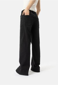 Melnas platās džinses, izgatavotas no denima. Iespējas ietver divas aizmugurējās kabatas un nedaudz saplēstu apakšmalu. Sader ar baltu augšu un sporta apaviem.