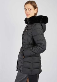 Czarna kurtka puchowa z kapturem z sztucznego futra, zapinaną na zamek kieszenią na piersi, elastycznym pasem i pikowanym wzorem, z akcentami z złotego metalu.