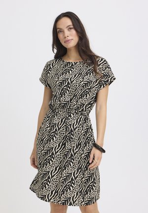 Frau mit langen dunklen Haaren, die ein knielanges Kleid mit kurzärmeligem schwarz-beigem Tierprint und ein schwarzes Armband trägt.