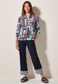 Blusa multicolorida con un patrón geométrico en tonos de negro, azul, rosa y blanco, con un cuello y mangas de tres cuartos. Pantalones amplios de talle alto en azul marino con puños doblados.