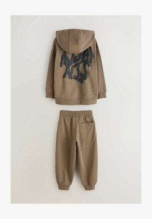 Pruun kapuutsiga dressipluus tekstureeritud musta graafilise tekstiga seljal, sobitatud samast kangast dressipükstega, millel on tagatasku ja elastne vöökoht.